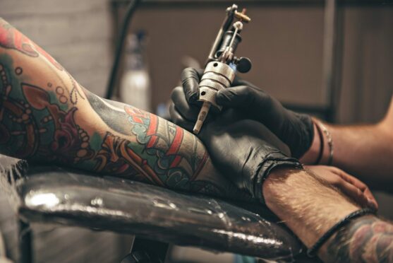 Tattoo artist with a tattoo gun, doing a tattoo on a person's forearm.
