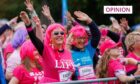 Women in pink wigs and Race for Life T shirts waving at the finish line of Race for Life Dundee in 2022.