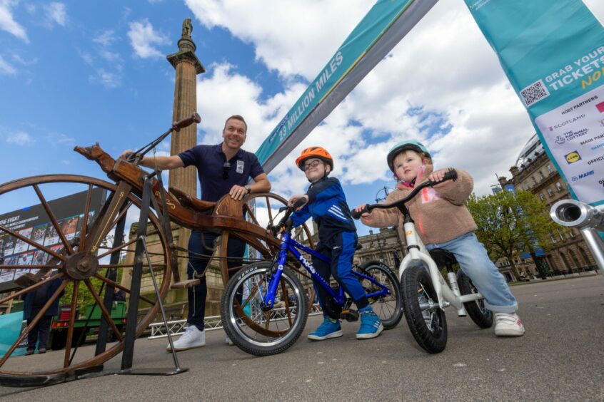 Sir Chris Hoy with a vintage bicycle and two small children on modern bikes in George Square, Glasgow.