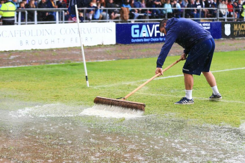 Groundsman Brian Robertson sweeps water off the pitch as torrential rain falls;. Image: David Young/Shutterstock