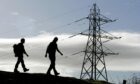 walkers silhouetted against sky with electricity pylons behind.