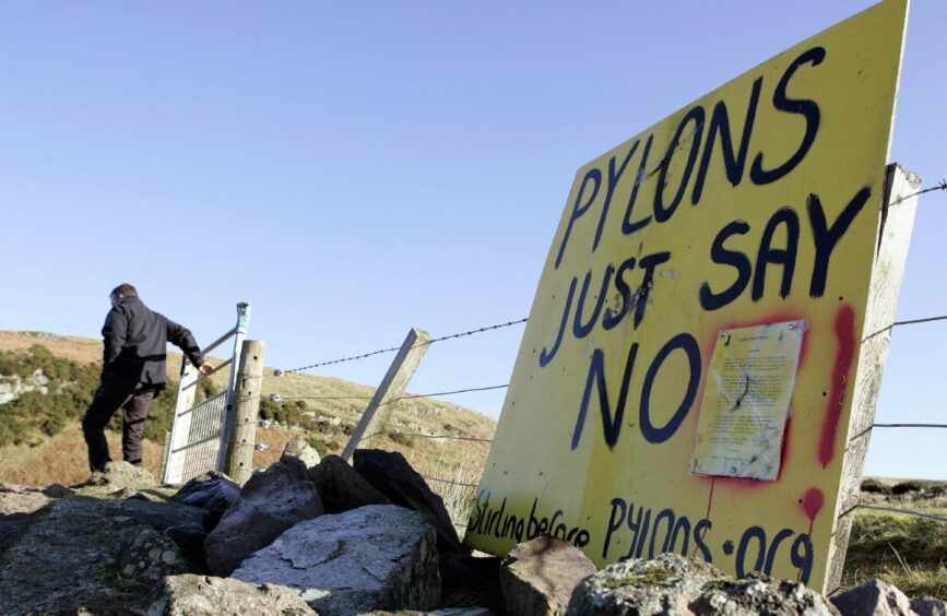 Man walking away from a placard which reads 'Pylons just say no' on Sheriffmuir.
