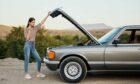A woman stands outside an old car with the hood open. Image used for article on scrappage scheme UK