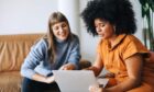 two women huddle over a laptop