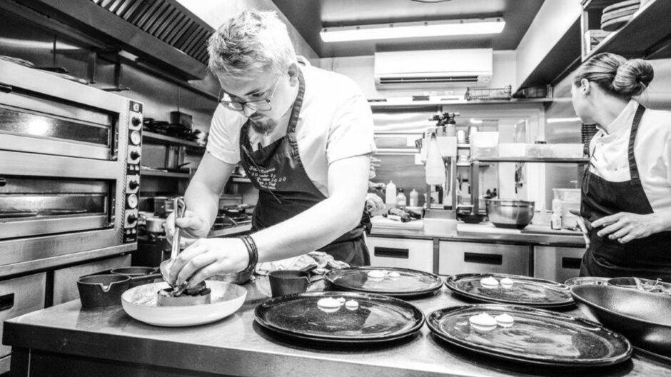 A black and white image of chef Jack Coghill in the kitchen plating dishes.