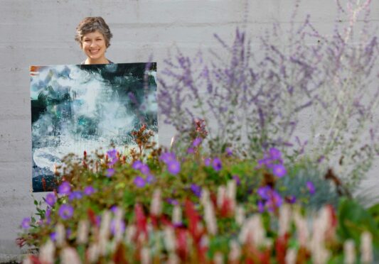 Libby Scott holding a large landscape painting in a garden.