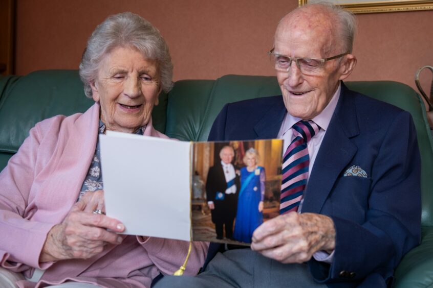 Ray and Lorna Armstrong seated on a sofa reading telegram with a photo of King Charles and Queen Camilla on the front.