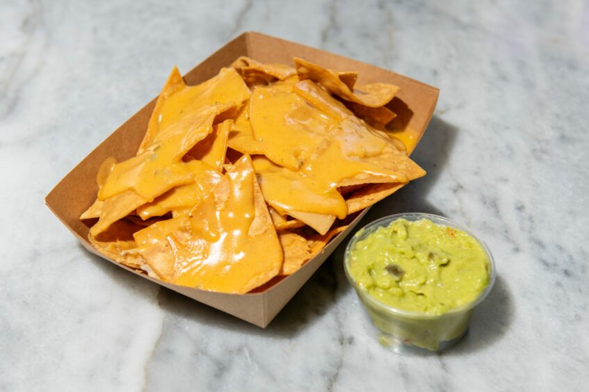 A tray of cheesy nachos with a pot of guacamole on the side at Wee Mexico.