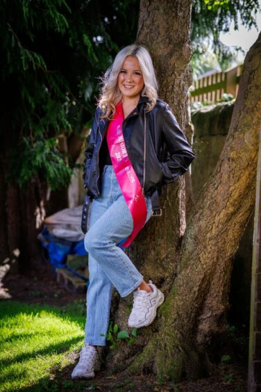 Mackenzie Connor leaning against tree in jeans and jacket in Kinross.