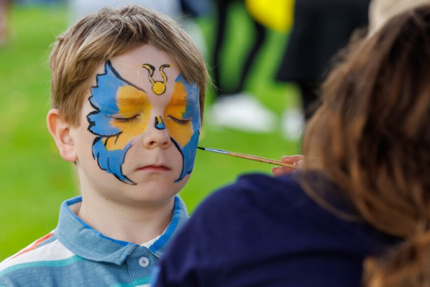 small boy having blue and yellow butterfly painted on his face.
