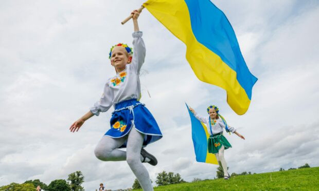 Two little girls running through park carrying Ukrainian flags.