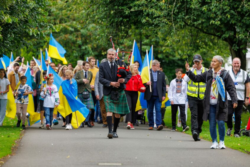 Piper leading parade of people carrying Ukrainian flags