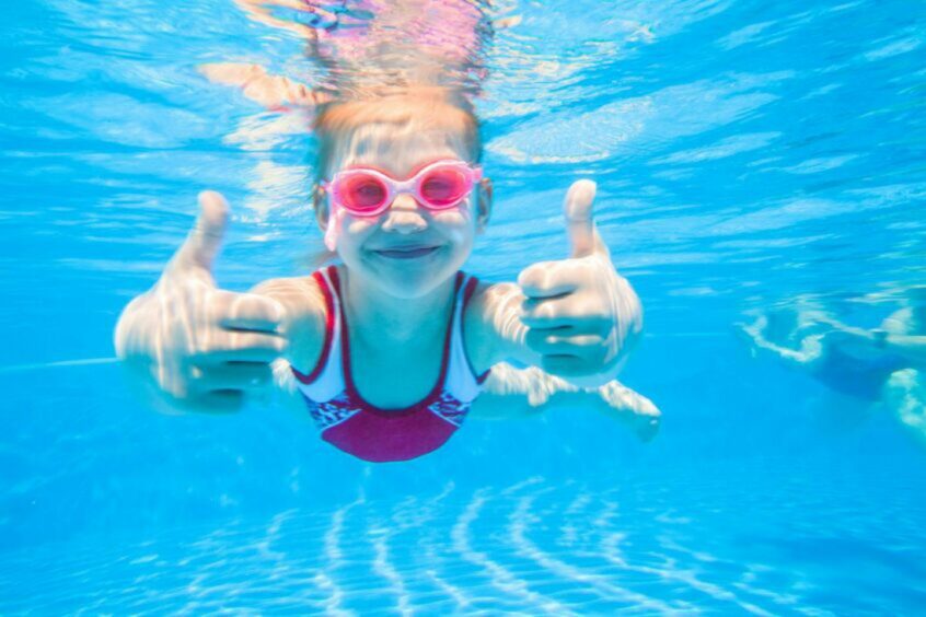 A wee girl swimming underwater giving two thumbs up.