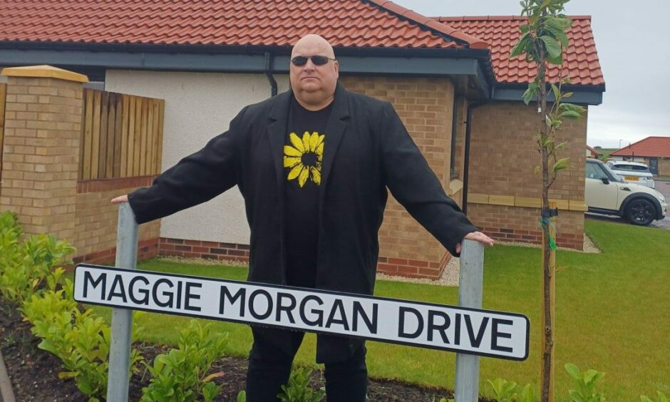 Lenny Low with the Maggie Morgan Drive sign in St Monans named after a 'witch.