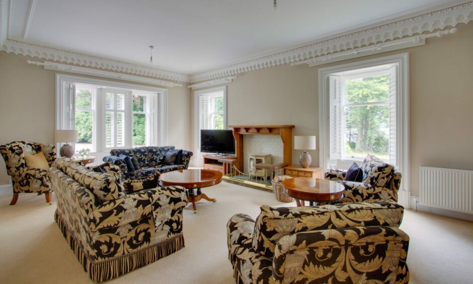A living area in Lintrathen House, with patterned couches, loveseats and armchairs, a fireplace and a television.