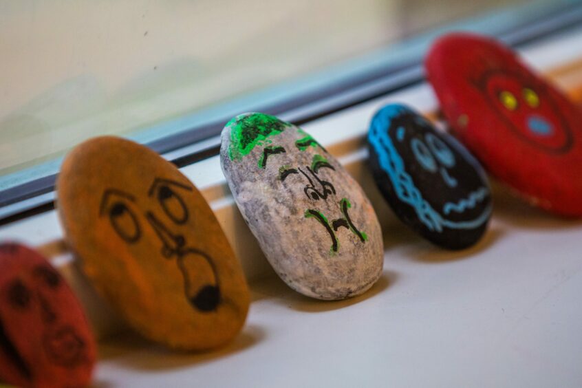Stones painted with colourful faces lined up against a window.