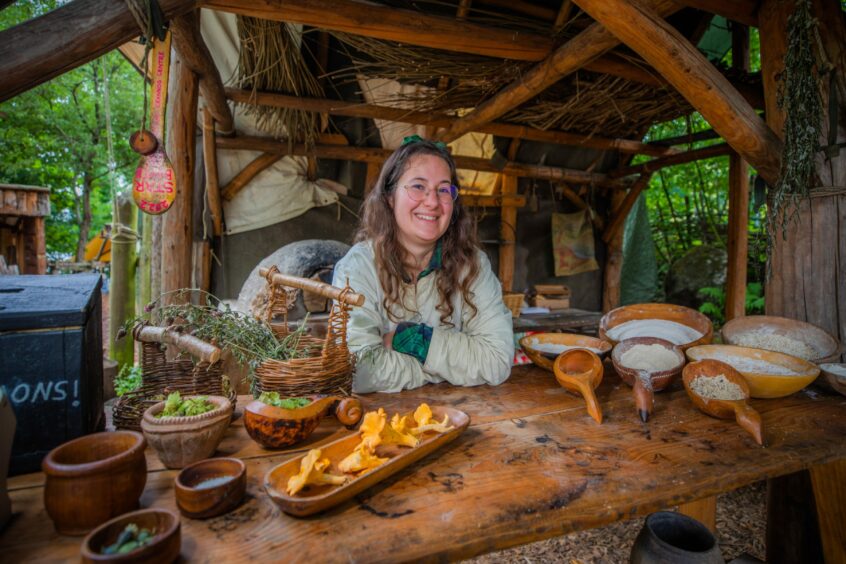 Jess Shaw, an Iron Age interpreter at the original Scottish Crannog Centre site, dressed in Iron Age clothing surrounded by cooking ingredients.
