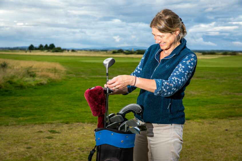 Image shows Sophie Mifsud with the golf clubs and bag she inherited from her Grandma. Sophie is at St Andrews Links and is choosing a club from the bag.