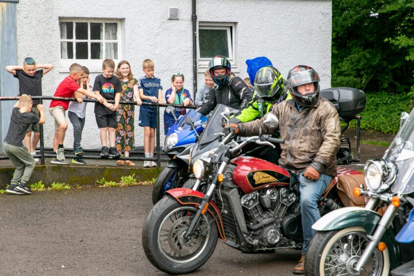 Bikers on motorbikes watched by children outside Luncarty village hall.