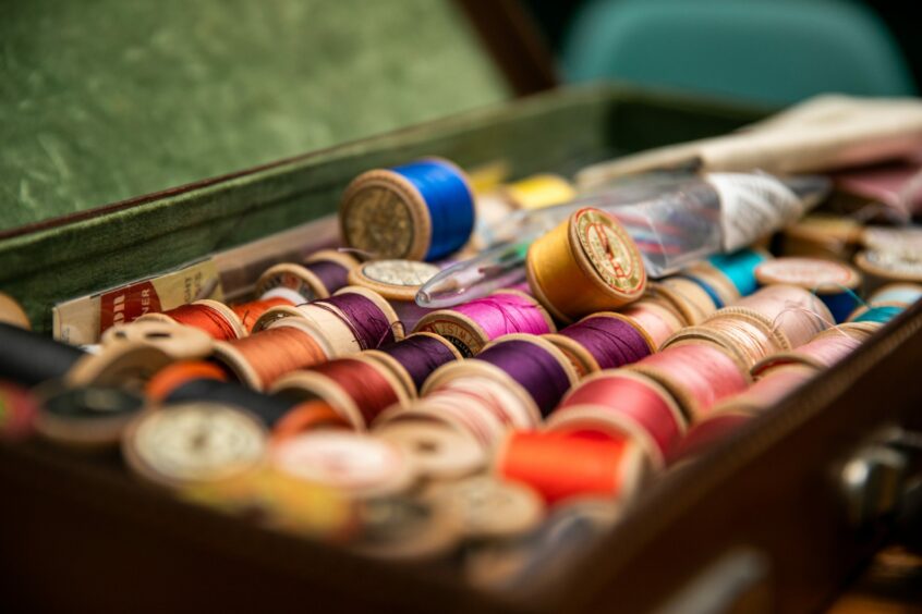 Image shows lots of old wooden spools with colourful thread in an old leather case.