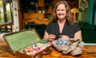 Image shows feature writer Nora McElhone sitting at a table with her Everyday Heirloom sewing case. The case is open showing colourful threads and she is sewing a Scout badge on an Explorers shirt.