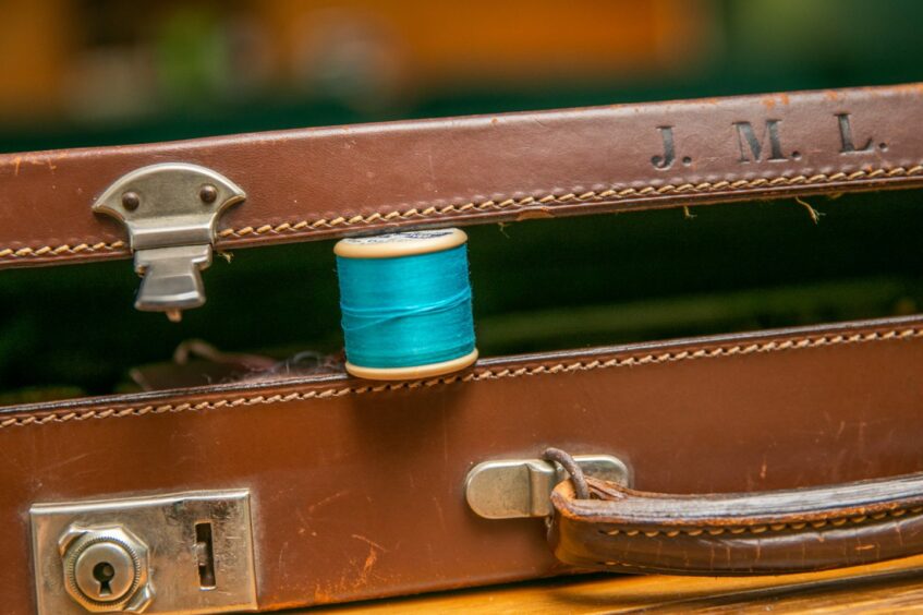 Image shows Nora McElhone's Everyday Heirloom - an old brown leather briefcase with the letters JML. The case is slightly open with a spool of turquoise thread visible.