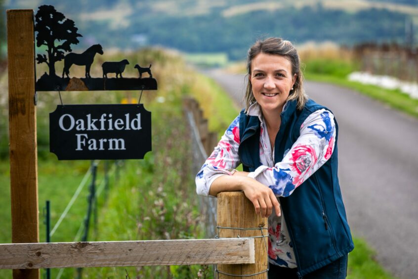 Tessa Sands standing next to sign for Oakfield Farm.