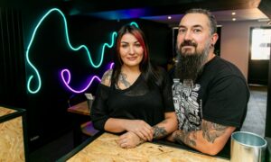 Nicola and Sian inside Ox & Anchor, in front of a black wall with neon lights.
