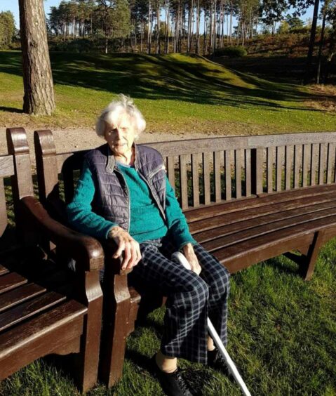 Image shows Sophie's Grandma Beatrice Jean Rowbotham. She is sitting on a bench at Sunningdale Golf Club and holding a white stick.