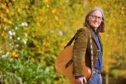 Dougie MacLean with guitar over his shoulder surrounded by autumn leaves.