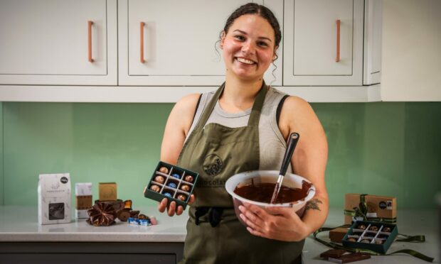 Chocolatier Chloe Oswald in her Chocolatia apron holding a bowl of chocolate and her 3-star Great Taste award collection.