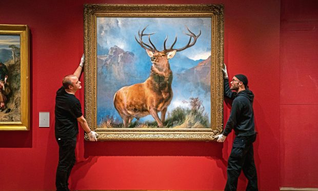 Image shows The Monarch of The Glen painting being hung in its new position by two gallery staff at the newly refurbished National Galleries of Scotland in Edinburgh.