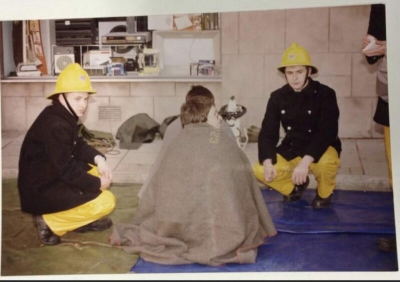 Chic training with fellow firefighter Alan Smith in the 1980s. The pair are kneeling next to a volunteer wrapped in a blanket.