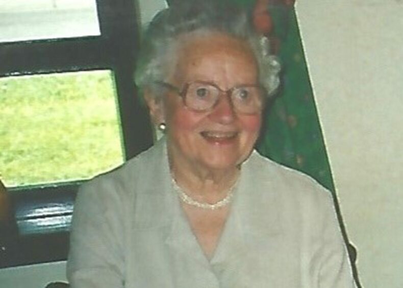 Image shows Jenny Milne aged 90. She is smiling, wearing glasses and has short white/grey hair.