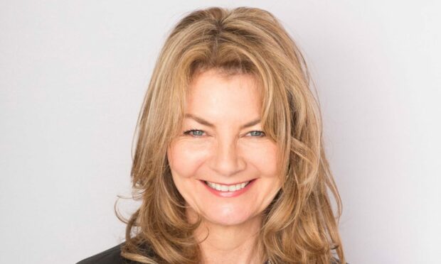 Image shows author of The Funny Thing About Death, Jo Caulfield. Jo is standing smiling with her shoulder length hair worn loose. She is wearing a striped blue and white t-shirt under a black leather jacket.