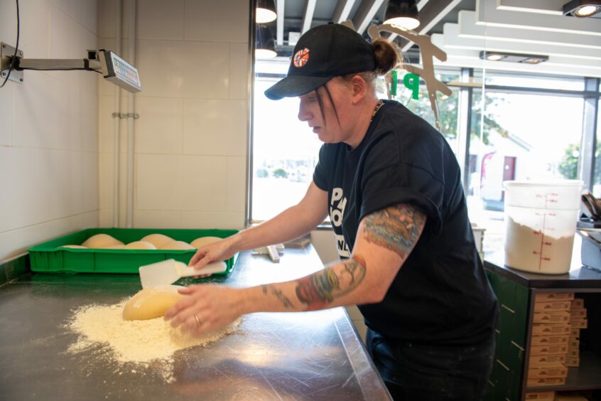 St Andrews pizza maker Sarah puts a dough ball in flour to turn it into a pizza base.