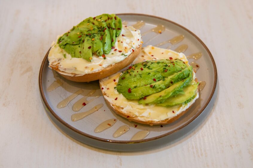 A plate of avocado, cream cheese and honey bagel.