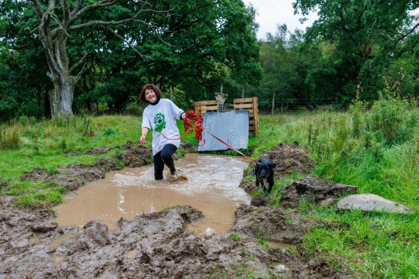 Morag Lindsay running through muddy puddle while Nancy the spaniel runs along the side.
