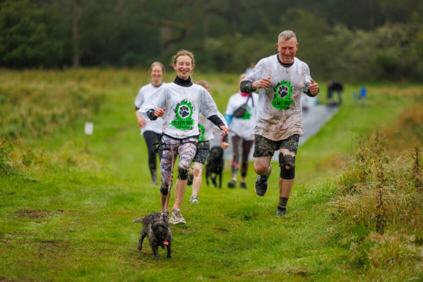 Group of runners, covered in mud with a small terrier dog running out in front at Auchingarrich.
