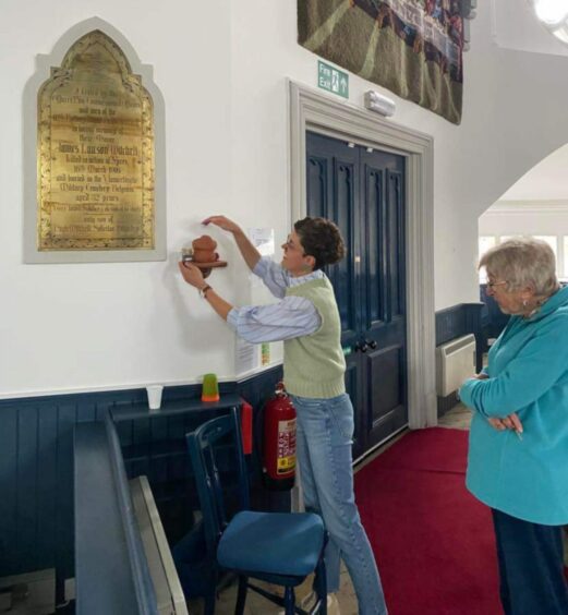 Marijke Vandevyvere places jar containing soil from Flanders next to plaque dedicated to Major Mitchell in Pitlochry Parish Church