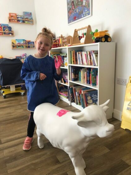 Pyper Rose Davidson, a CHAS sibling, next to small cow sculpture