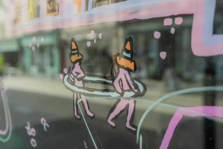 Illustration on Perth shop window showing two figures with traffic cones on their heads, standing in a ring. The design is a reference to the famous statue in Perth High Street.