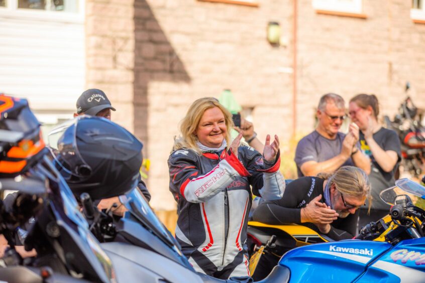 Woman in bikers leathers smiling and applauding.