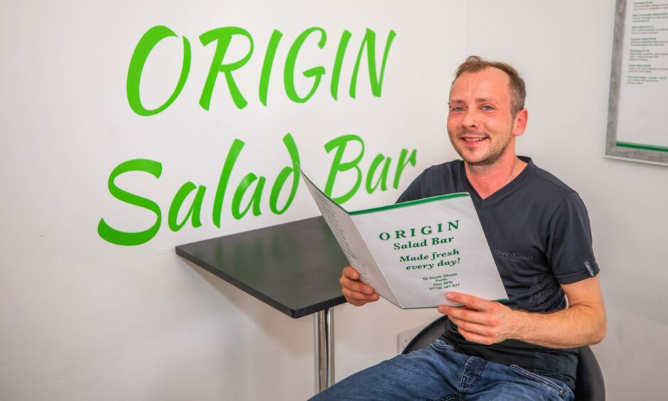 Ethan March sitting inside Origin salad bar holding a menu