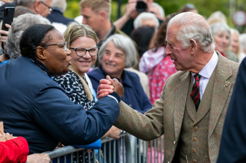 King Charles in a warm handshake with a crowd member in Kinross