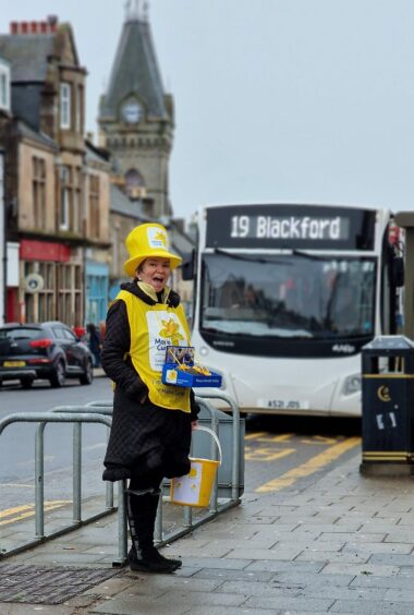 Estelle Nicol wearing yellow tabard and daffodil hat collecting for Marie Curie in Auchterarder high street.