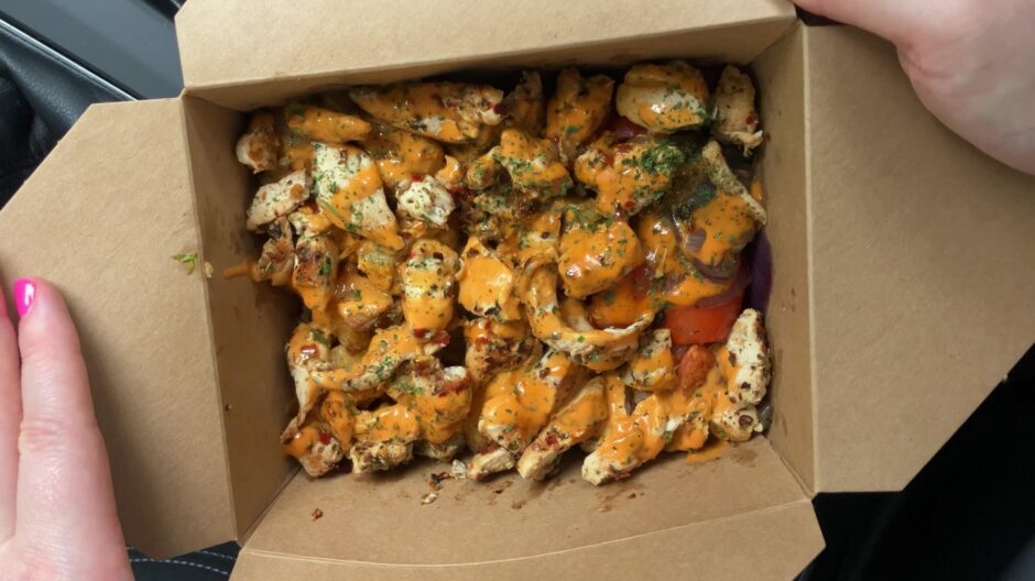 A takeout box with chicken, vegetables and sauce