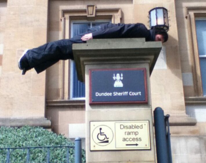 Man planking on Dundee Sheriff Court sign.