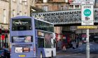 A bus goes down a street with a Low Emission Zone sign