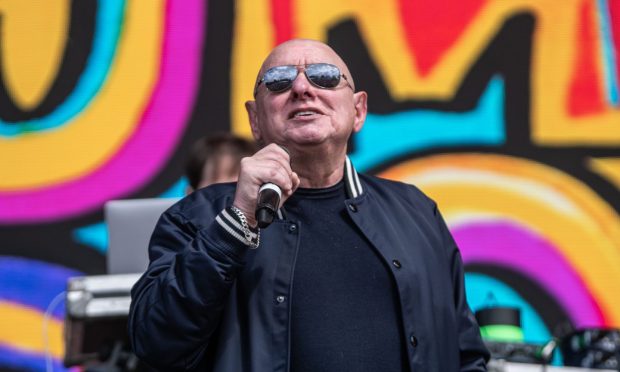 Shaun Ryder, wearing sunglasses and performing on stage in 2023.